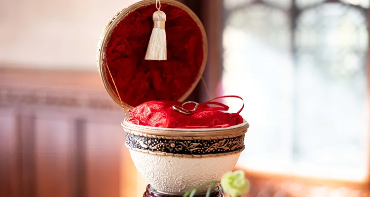 Two rings in a ringbox made from a goose egg, red cushion and lace interior with cream, black and gold embellishments on the exterior.