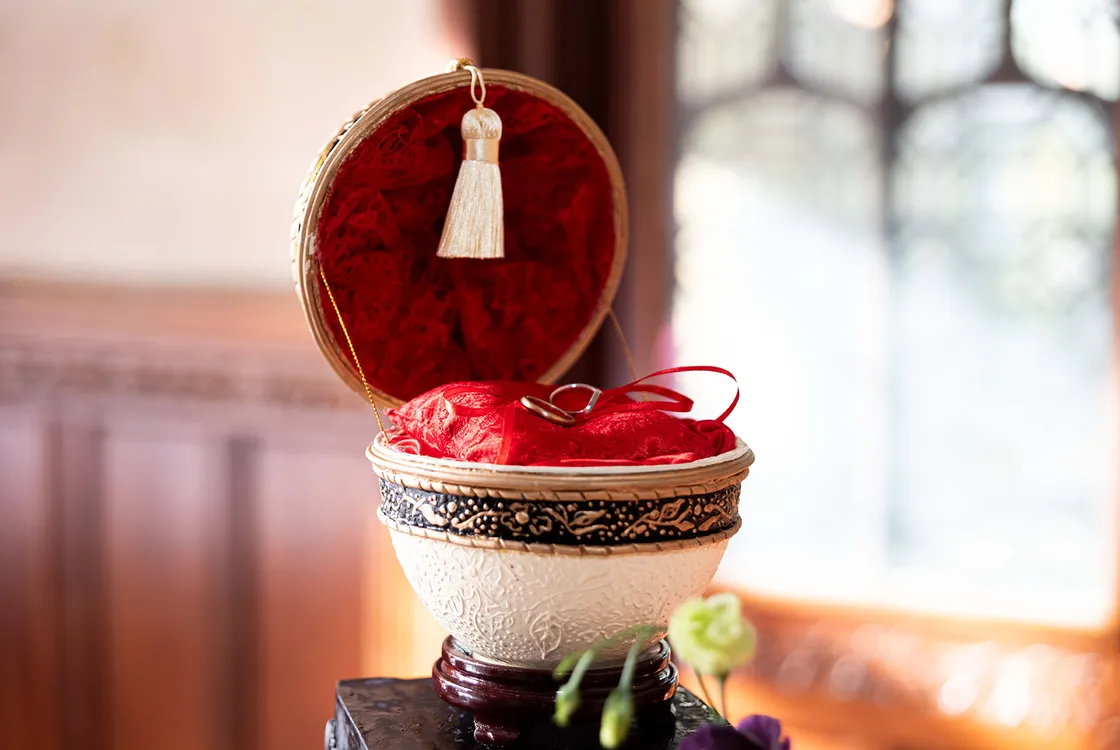 Two rings in a ringbox made from a goose egg, red cushion and lace interior with cream, black and gold embellishments on the exterior.