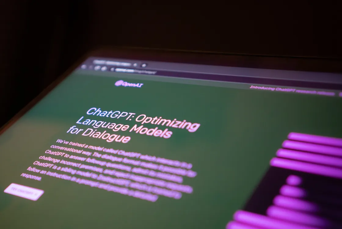 A close up of a computer screen showing the OpenAI website with a blurry background