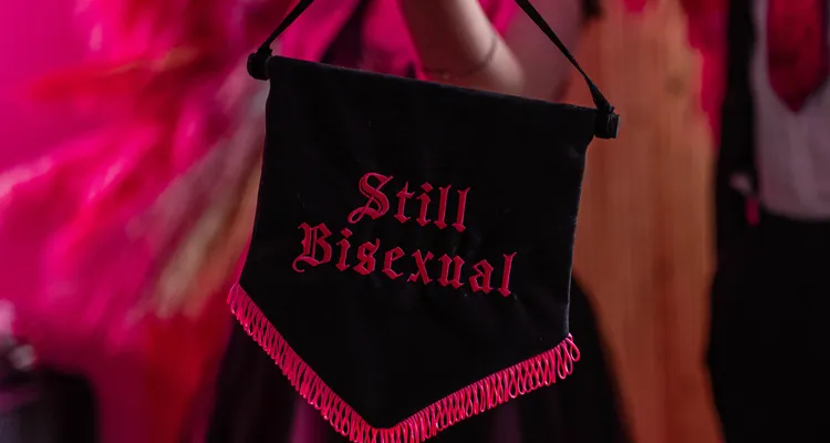 A black banner with pink fringing along the bottom with 'still bisexual' written in pink in the centre