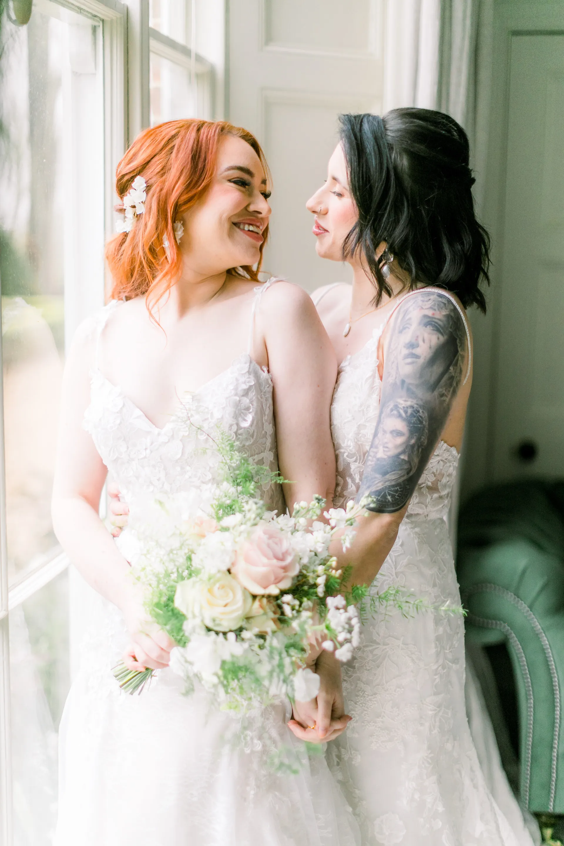A couple hugging in front of a window, holding a wedding bouquet
