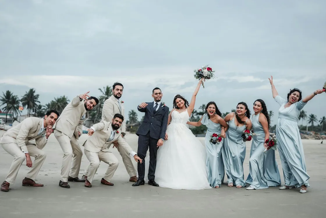 a bride, groom and their wedding party standing next to each other on a beach, celebratory poses and excited faces