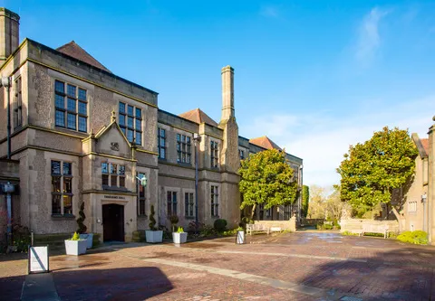 The frontage of a gothic hall with trees and planters