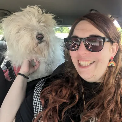 Rachel in a passenger seat of a car with a white dog over their shoulder