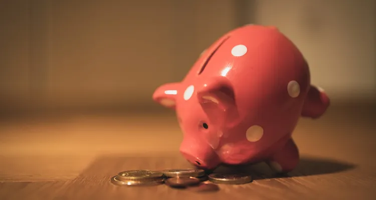 A piggy bank on a table with it's nose tilted towards some coins