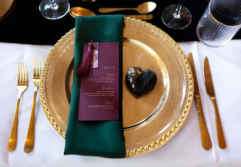 A table setup with gold cuterly with the menu on top of a black napkin