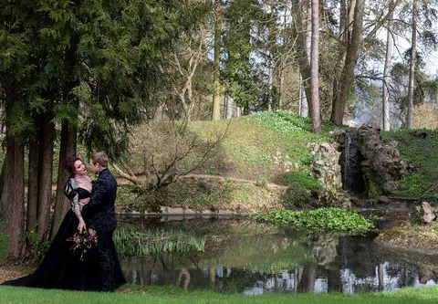 A couple, dressed in black, stand in front of a lake